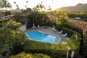 A swimming pool surrounded by lush greenery and palm trees, with lounge chairs and a view of a mountainous landscape. - Plantation Hale Suites (Kapaa)
