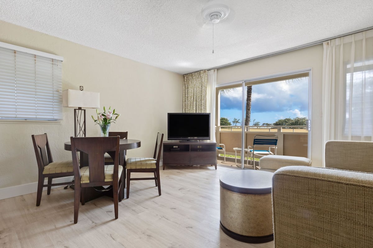 A hotel room with a dining area, a television, a balcony with a view, and a ceiling fan.