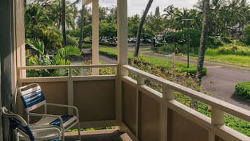 Un espacio de estar al aire libre con techo, sillas y vista a una calle con palmeras.