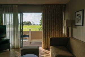 Una habitación con sofá, televisión, lámpara y vistas a un paisaje verde a través de un ventanal.