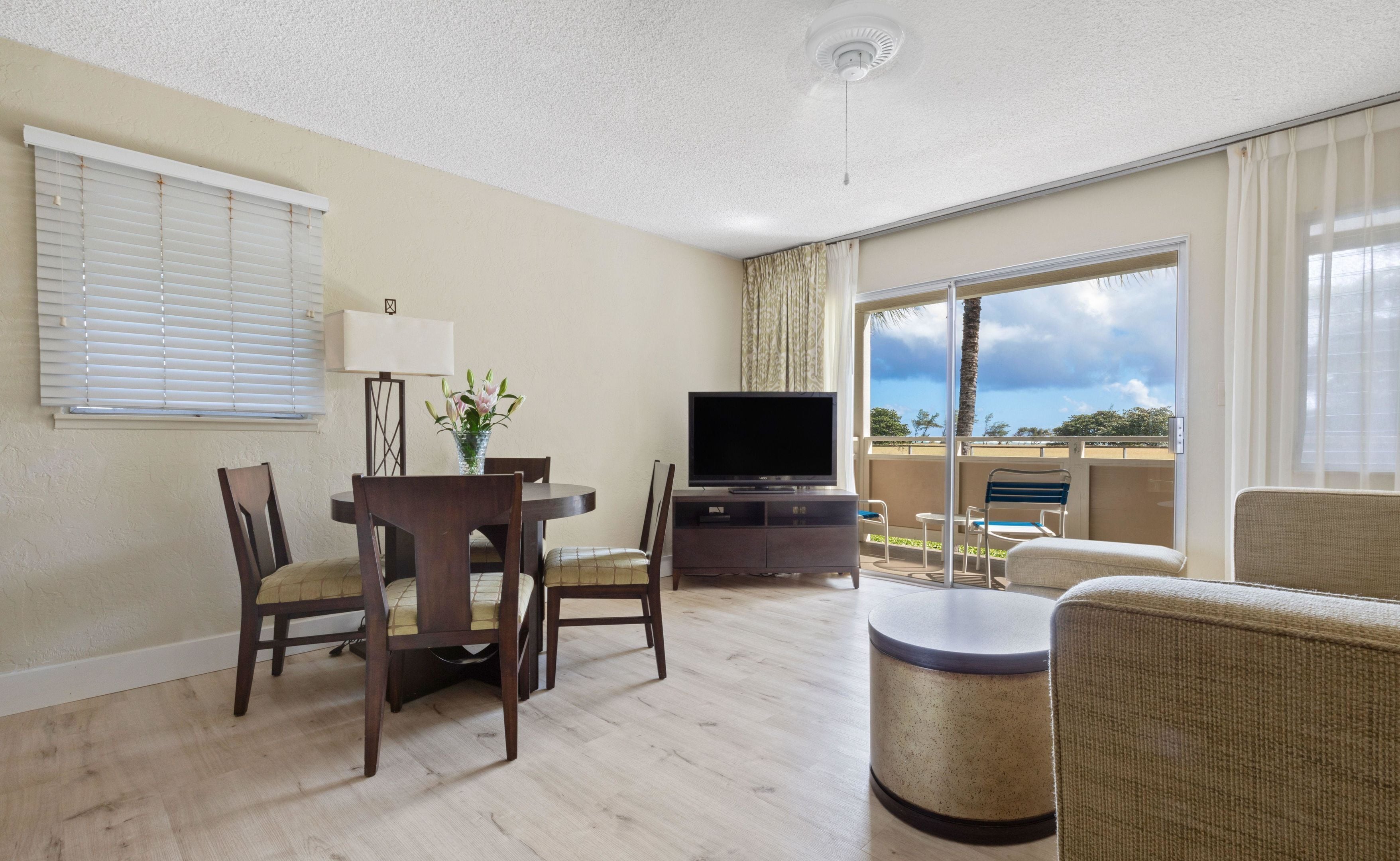 A hotel room with a dining area, a television, a balcony with a view, and a ceiling fan.