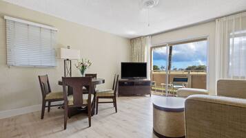 A hotel room with a dining area, a television, a balcony with a view, and a ceiling fan.