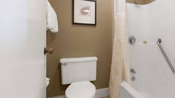 A bathroom with a toilet, a framed picture on the wall, a shower curtain, and a bathtub.