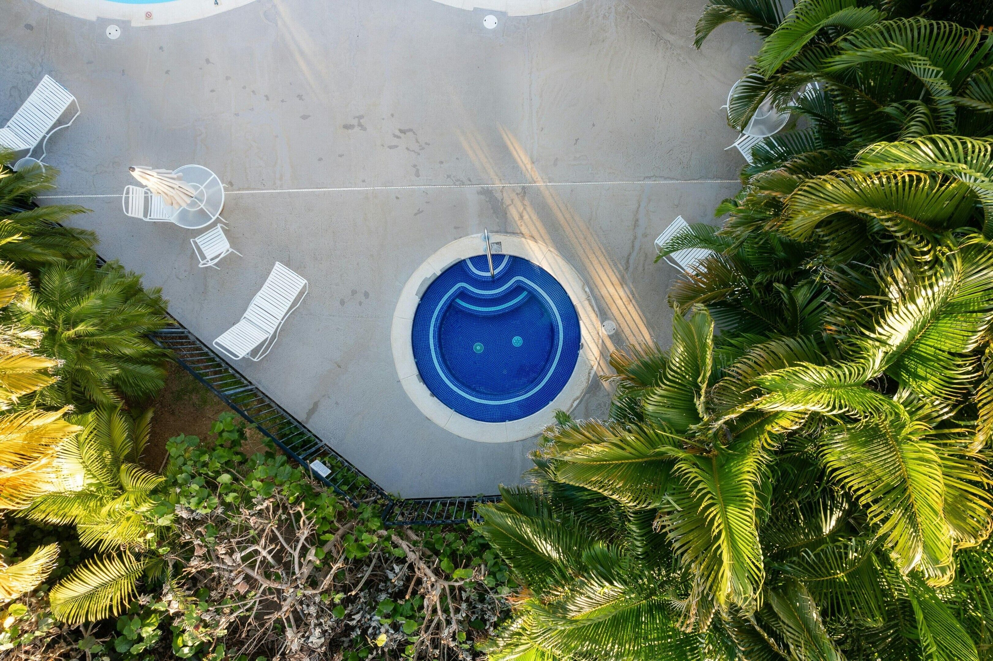 A circular pool with a blue center, surrounded by white lounge chairs and a metal fence.