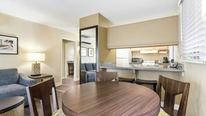 Habitación de hotel con comedor, kitchenette y sala de estar con sofá y lámpara.
