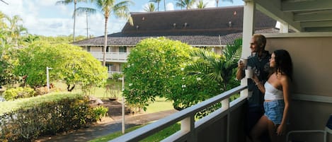 A balcony with a view of a building, greenery, and palm trees.