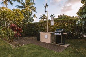 A patio area with a grill, trash bins, and a signpost. - Plantation Hale Suites (Kapaa)