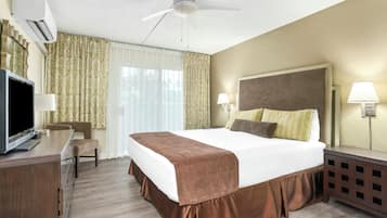 A hotel room with a bed, a desk with a television, a ceiling fan, and two bedside lamps.