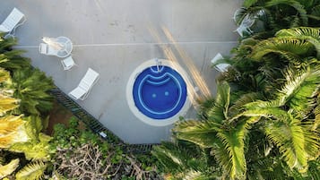 A circular pool with a blue mosaic design, surrounded by white lounge chairs and a small table.