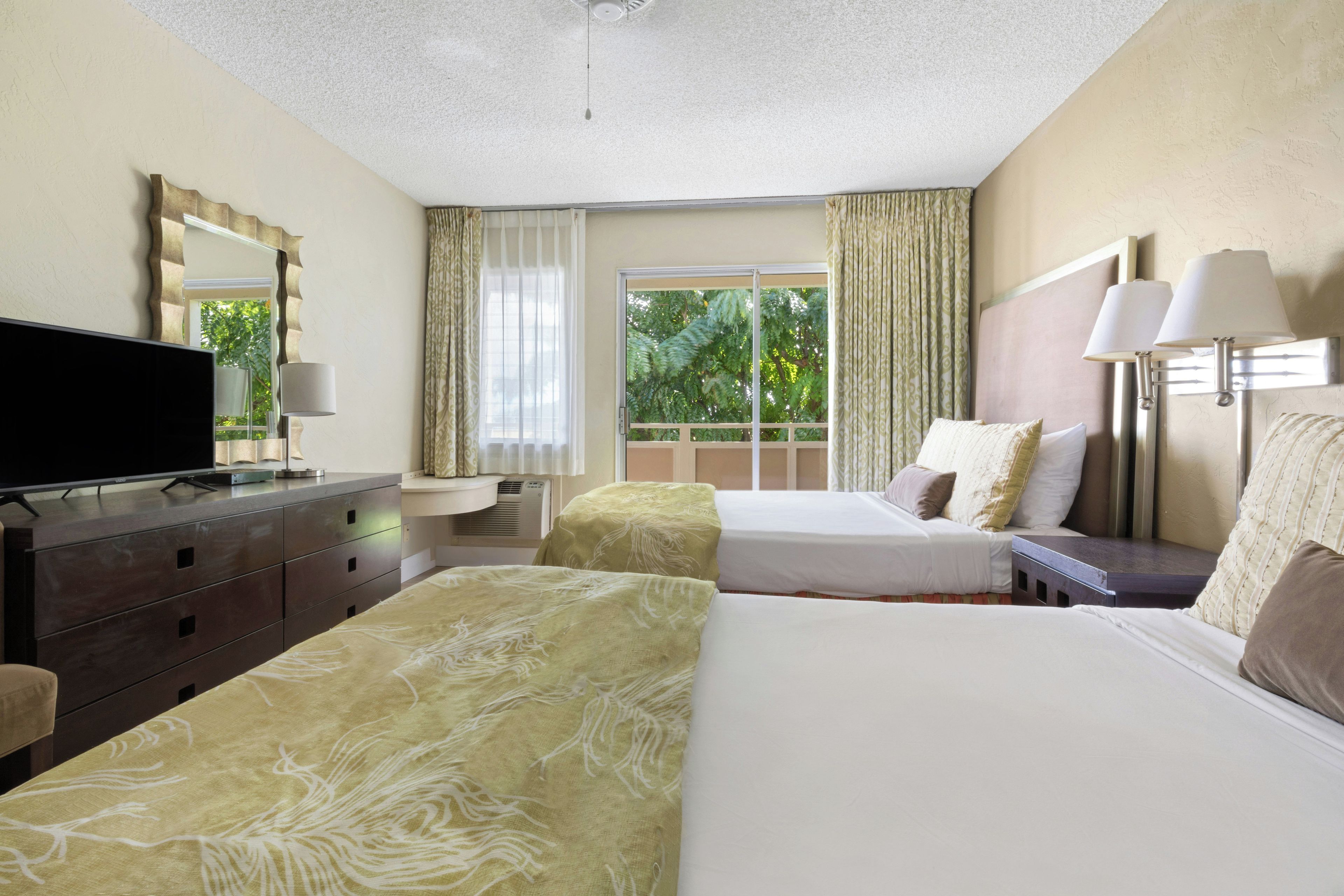 A hotel room with two beds, a television, a desk, and a window with curtains.