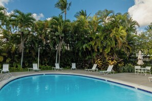 A swimming pool with lounge chairs and umbrellas, surrounded by palm trees.