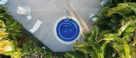 Una piscina circular con diseño de mosaicos azules, rodeada de sillas reclinables blancas y una pequeña mesa.