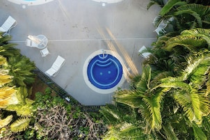 Una piscina circular con diseño de mosaicos azules, rodeada de sillas reclinables blancas y una pequeña mesa.