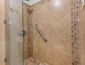 Una ducha con puerta de cristal, paredes de azulejos y un pasamanos.