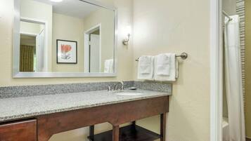 A bathroom with a granite countertop, a wooden vanity, a mirror, and a towel rack.