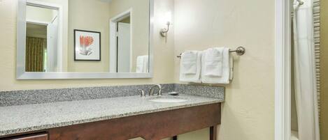 A bathroom with a granite countertop, a wooden vanity, a mirror, and a towel rack.