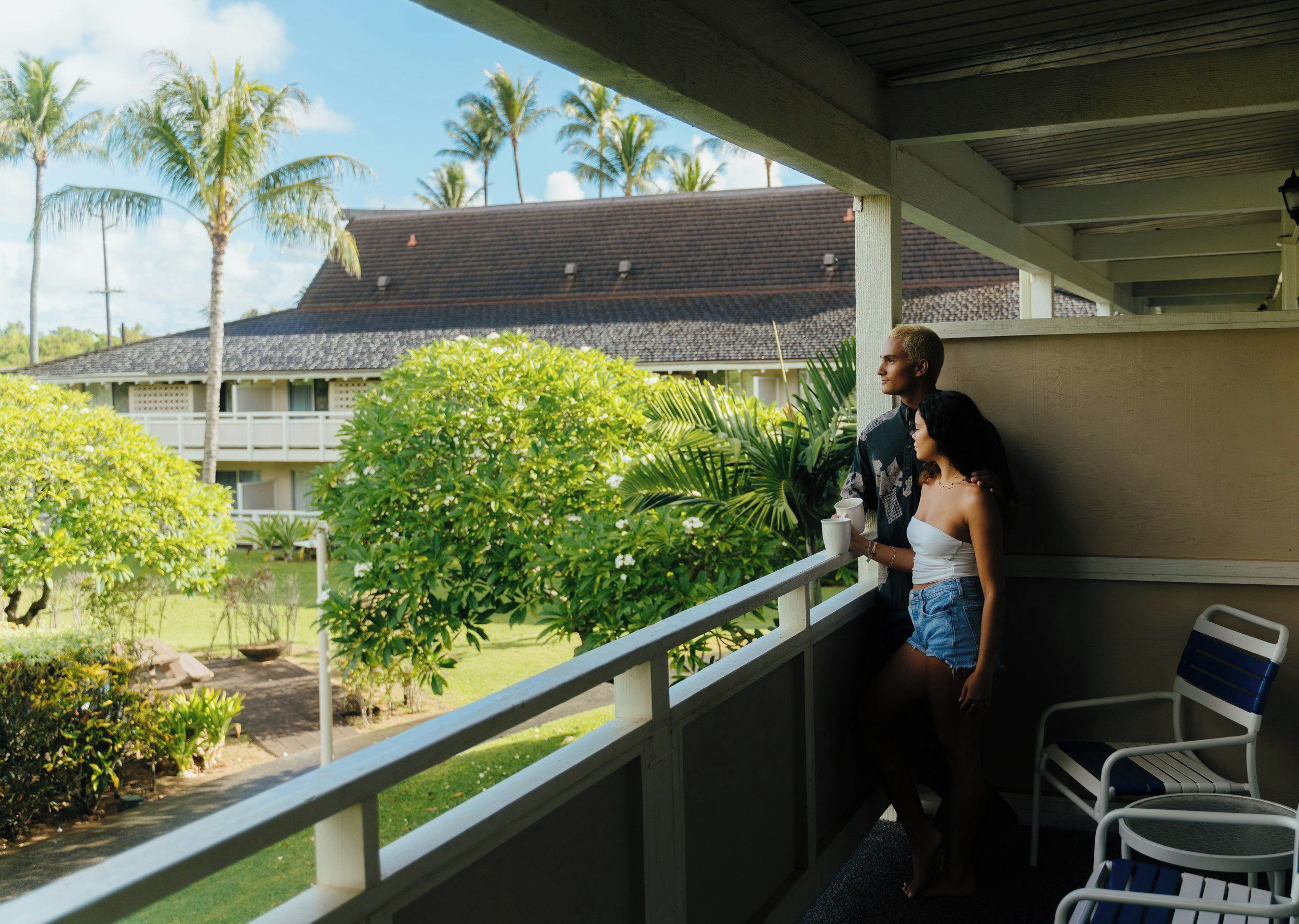 A balcony with a view of a building with a tiled roof and palm trees.