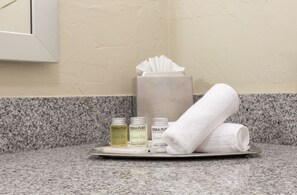 Una encimera de baño con una toalla, una caja de pañuelos y tres botellas de productos Terra Pure.