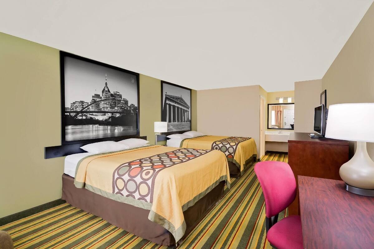 A hotel room with two beds, a desk, a chair, and a television.