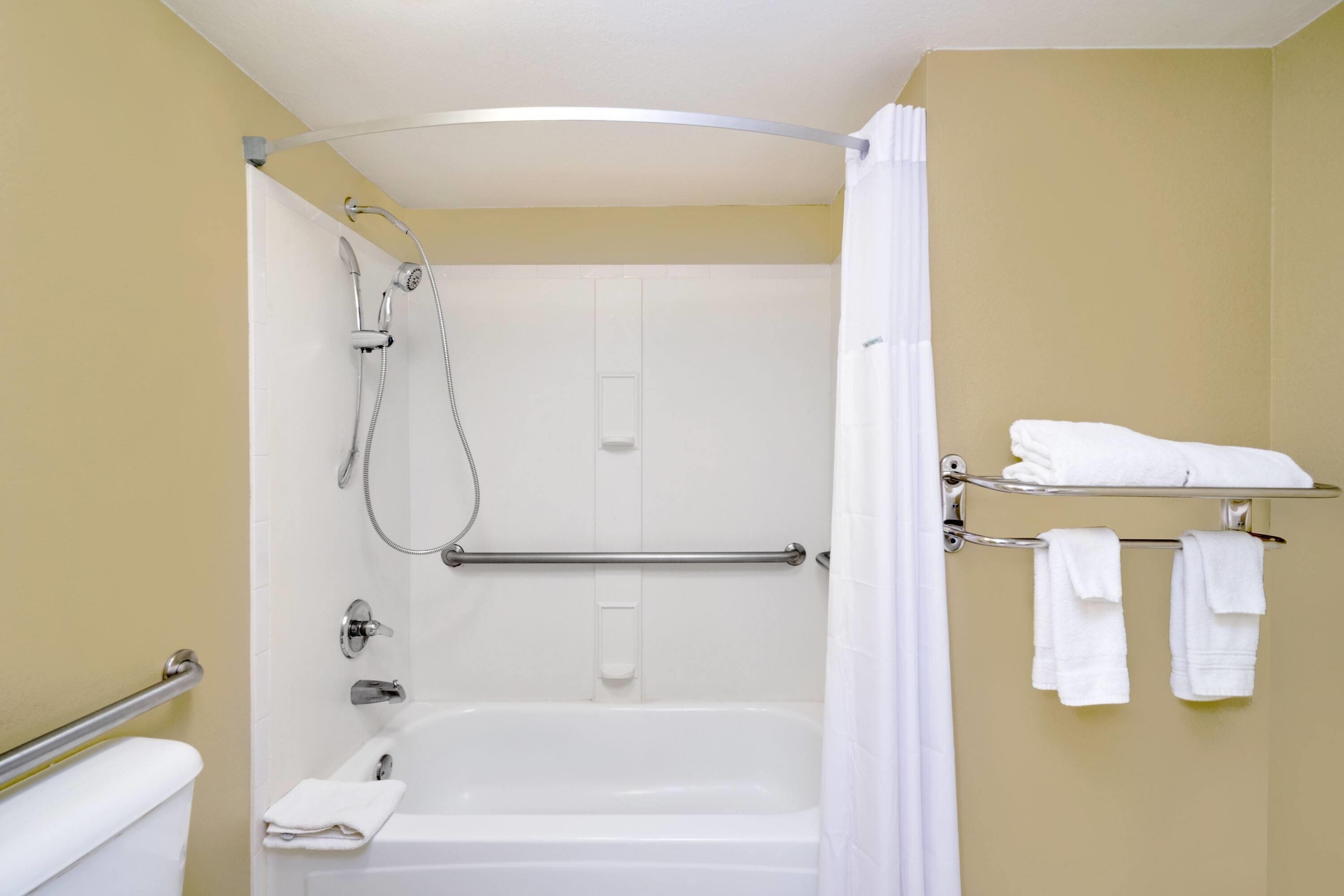 Un baño con bañera, ducha, toallero y toallas, además de una barra de apoyo.