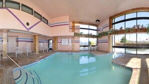 An indoor swimming pool with clear water, surrounded by a tiled floor and equipped with a pool ladder. There are several white chairs and tables around the pool area, and the walls are decorated with stripes and wooden panels. - Super 8 by Wyndham Hermitage Nashville (Hermitage)