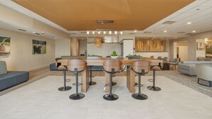 A modern dining area with a wooden table and bar stools, a sofa, and a decorative hanging light fixture. - Kozy Hotel Dallas DFW Airport Area West (Bedford)