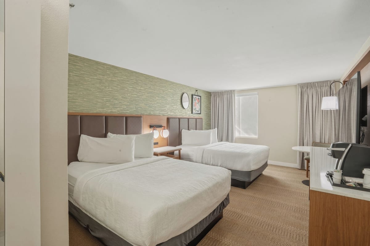A hotel room with two beds, a desk, a chair, a TV, and a window with curtains.