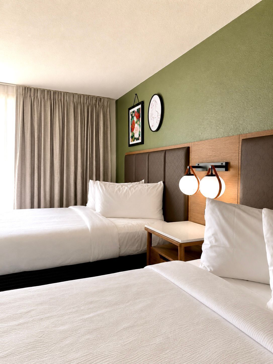 Habitación de hotel con dos camas, una mesita pequeña, una lámpara fijada a la pared y un cuadro enmarcado.