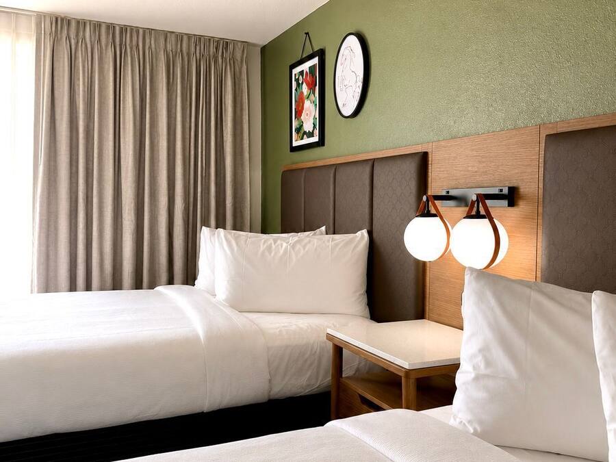 Una habitació d'hotel amb dos llits, una taula petita, una làmpada subjecta a la paret i un quadre amb marc.