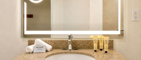 A bathroom with a large mirror, a sink, and toiletries.
