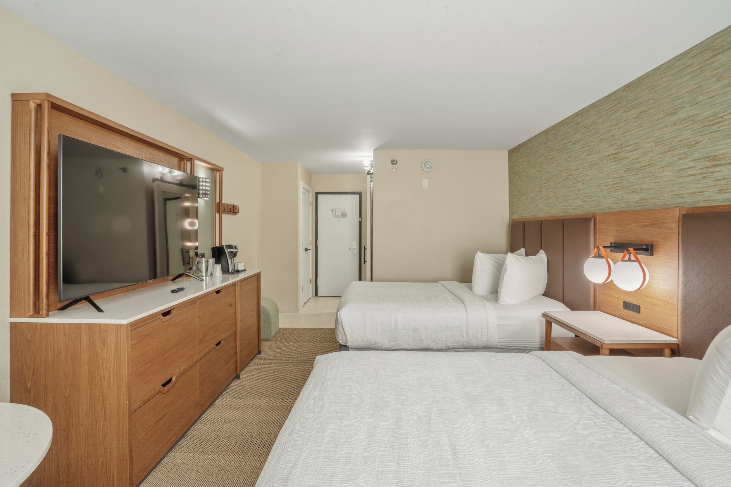 A hotel room with a large bed, a TV, a dresser, and a bedside table with lights.