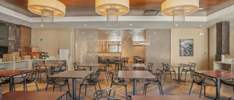 A spacious dining area with multiple tables and chairs, wooden flooring, and modern pendant lighting.