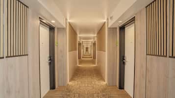 A hotel corridor with wooden paneling, a patterned carpet, and doors marked with room numbers.