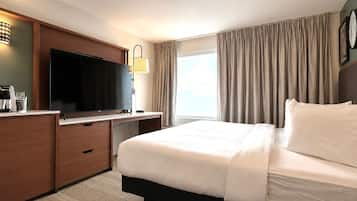 Habitación de hotel con una cama grande, un televisor de pantalla plana, un escritorio con cafetera y una ventana con cortinas.