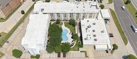 A multi-story hotel with a rooftop pool, parking lot, and adjacent road.