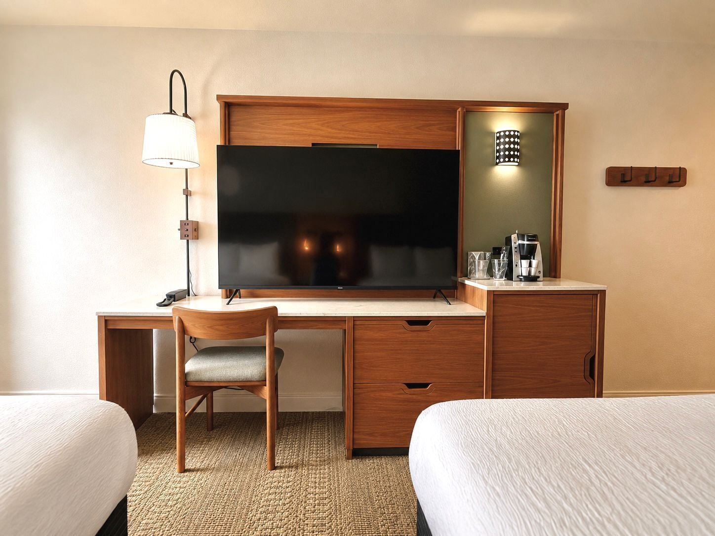 A hotel room with a wooden desk, a television, a lamp, a coffee maker, and two beds.