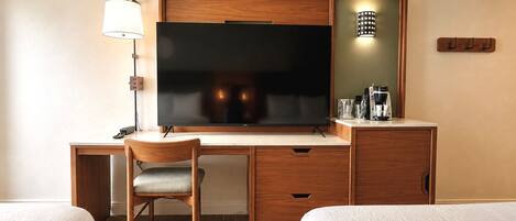 A hotel room with a wooden desk, a television, a lamp, a coffee maker, and two beds.
