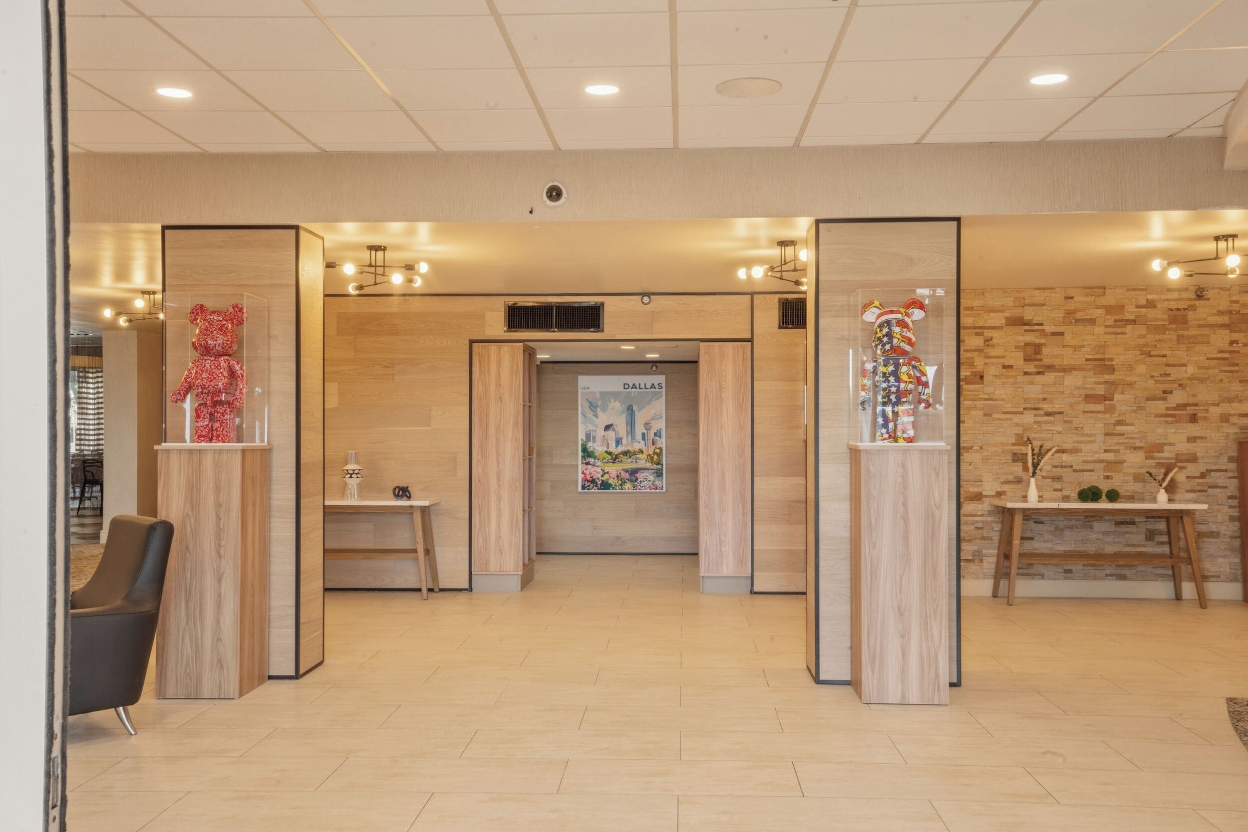 A modern hotel lobby with wooden flooring, a reception desk, and two decorative glass panels with figurines.