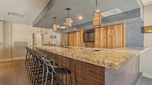 A kitchen with a granite countertop, wooden cabinets, bar stools, pendant lights, and a stainless steel range hood. - Kozy Hotel Dallas DFW Airport Area West (Bedford)