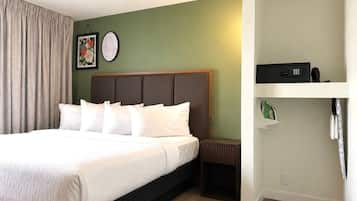 A hotel room with a bed, a nightstand, a wall clock, and a shelf with a remote control.