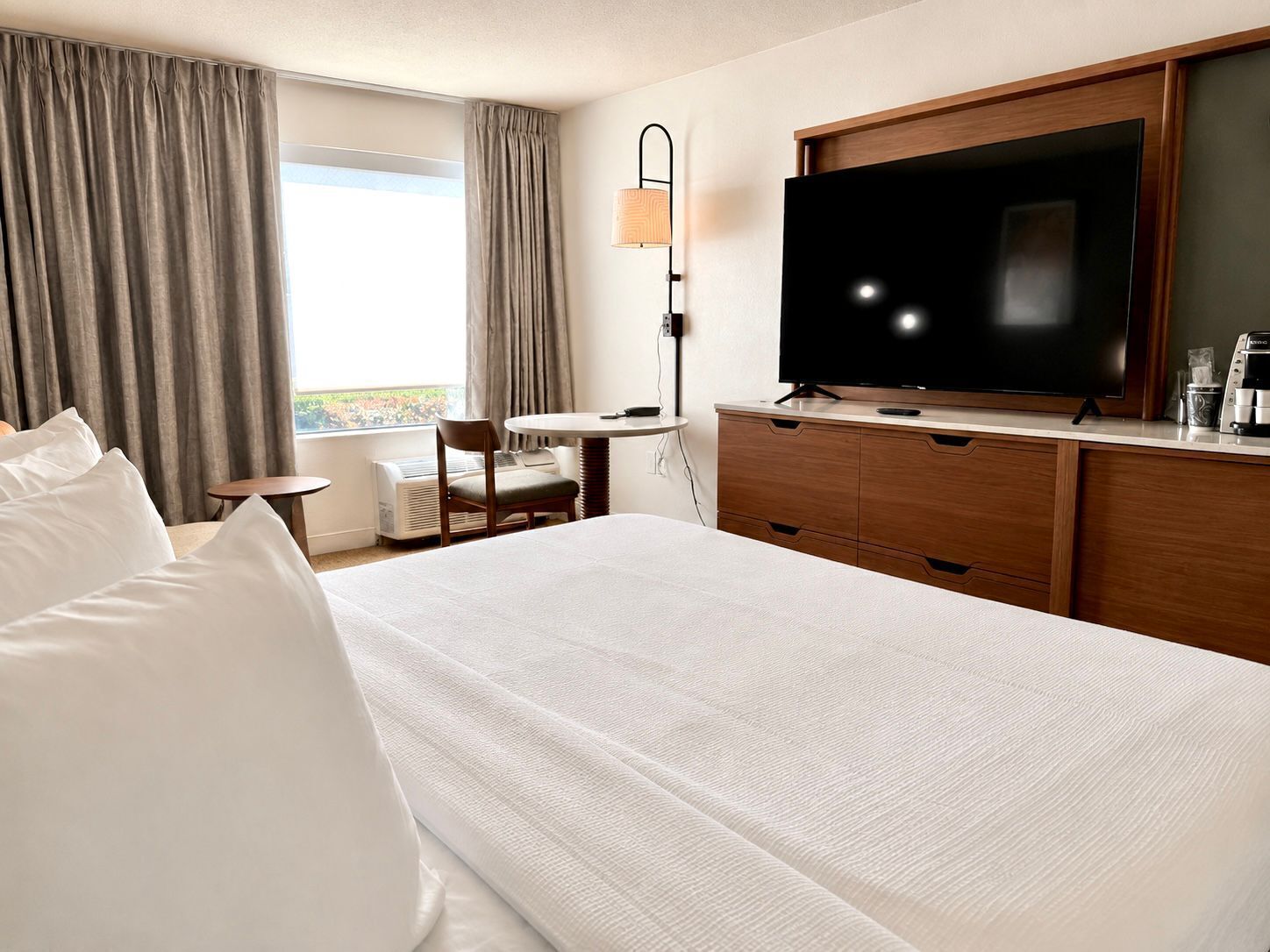 A hotel room with a bed, a TV, a desk, and a chair.