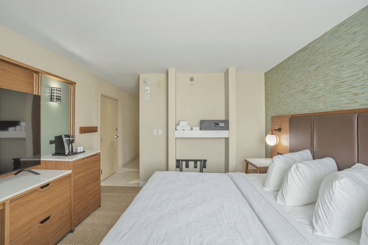 A hotel room with a bed, a desk, a mirror, a television, and a small table.
