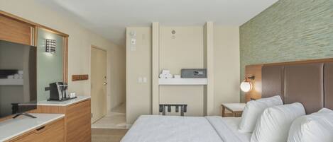 A hotel room with a bed, a desk, a mirror, a television, and a small table.