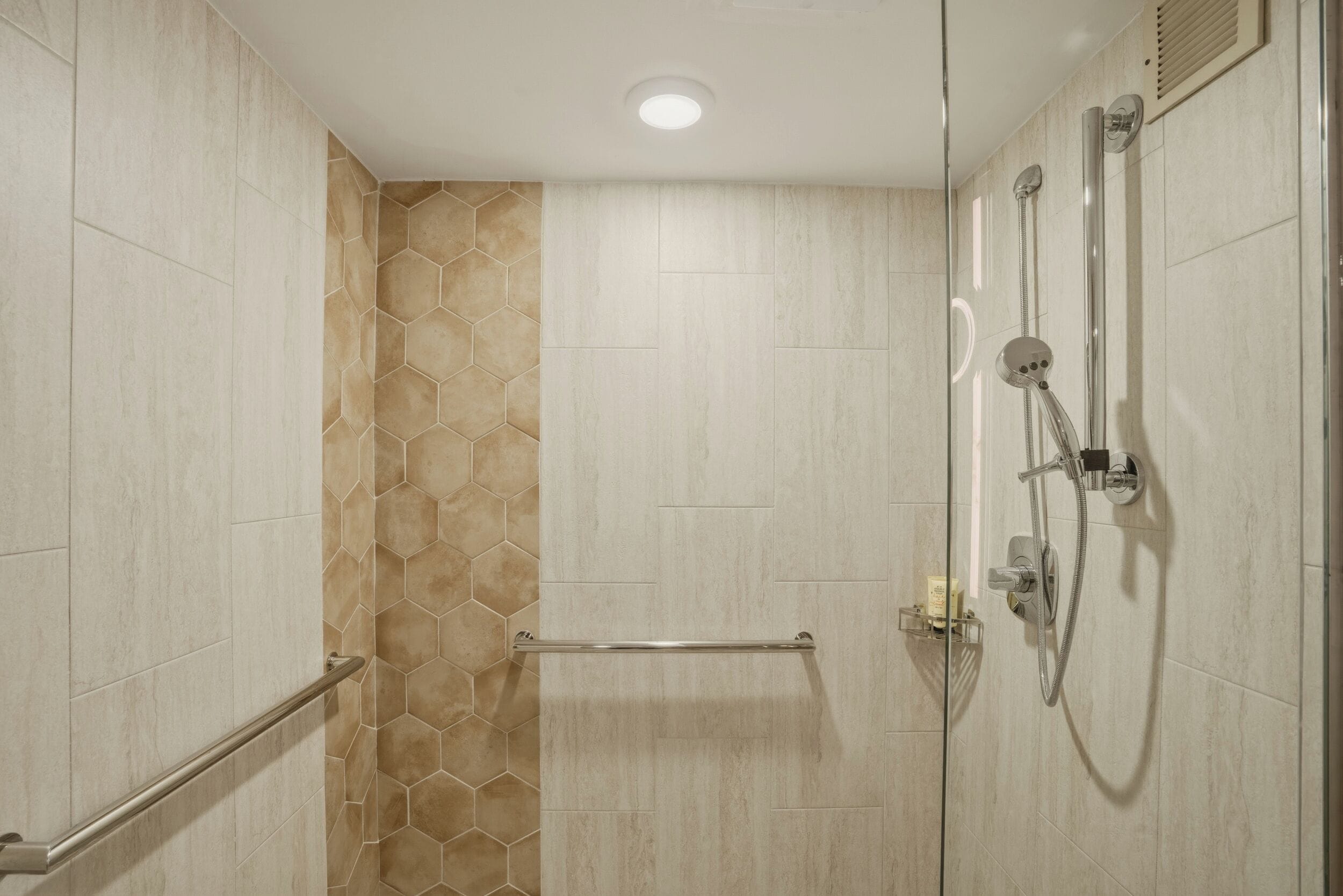 A shower area with a glass partition, a handrail, a showerhead, and a towel rack.