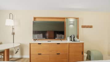A hotel room with a wooden dresser, a mirror, a desk, and a lamp.