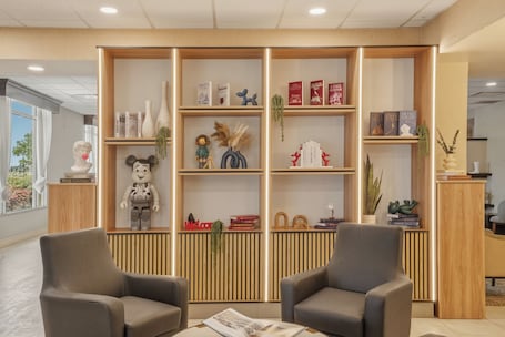 A modern interior with a wooden bookshelf, two grey armchairs, and a magazine on a table.