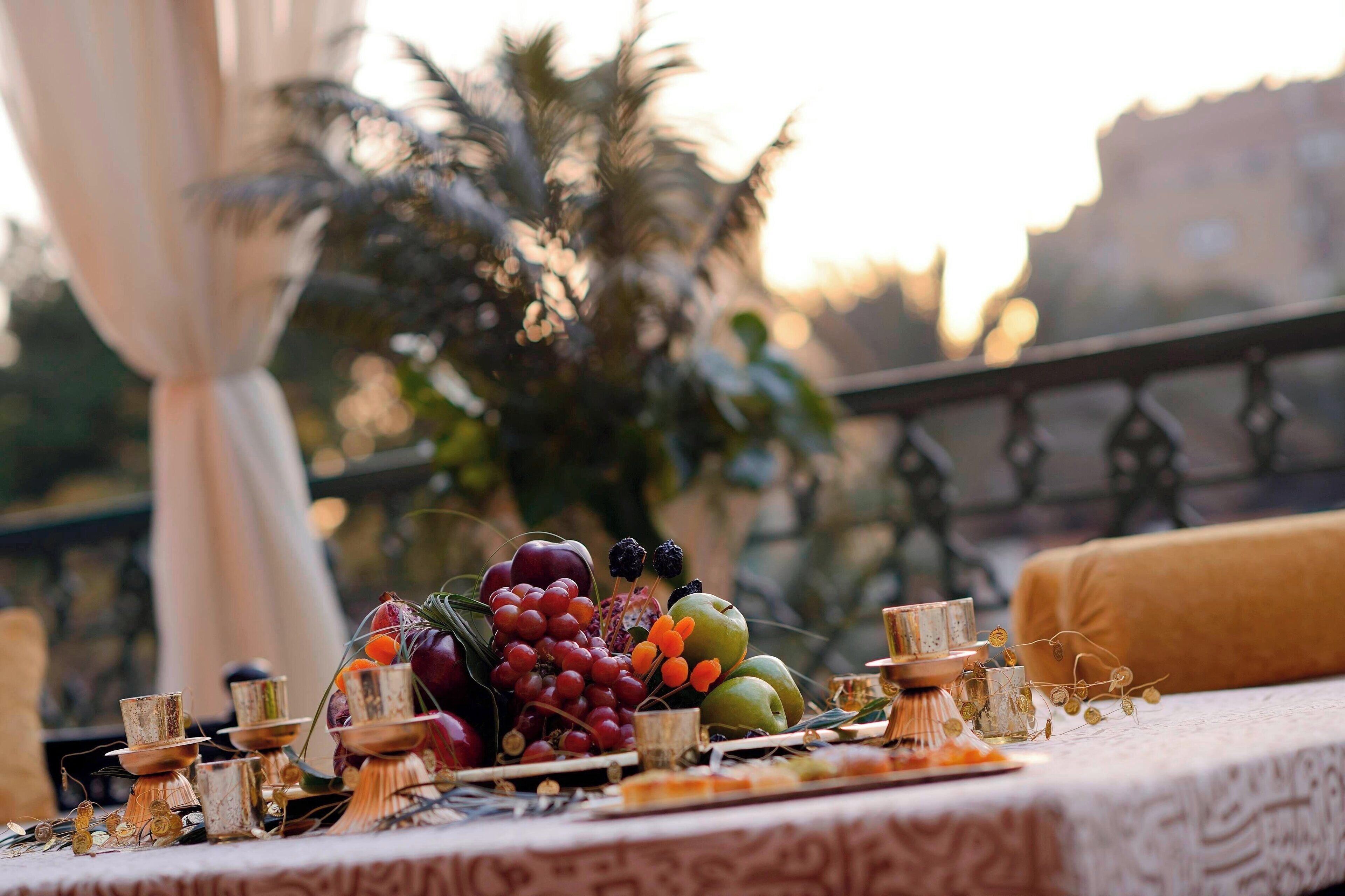 Un tavolo con frutta, candele e vista su palme e edifici.