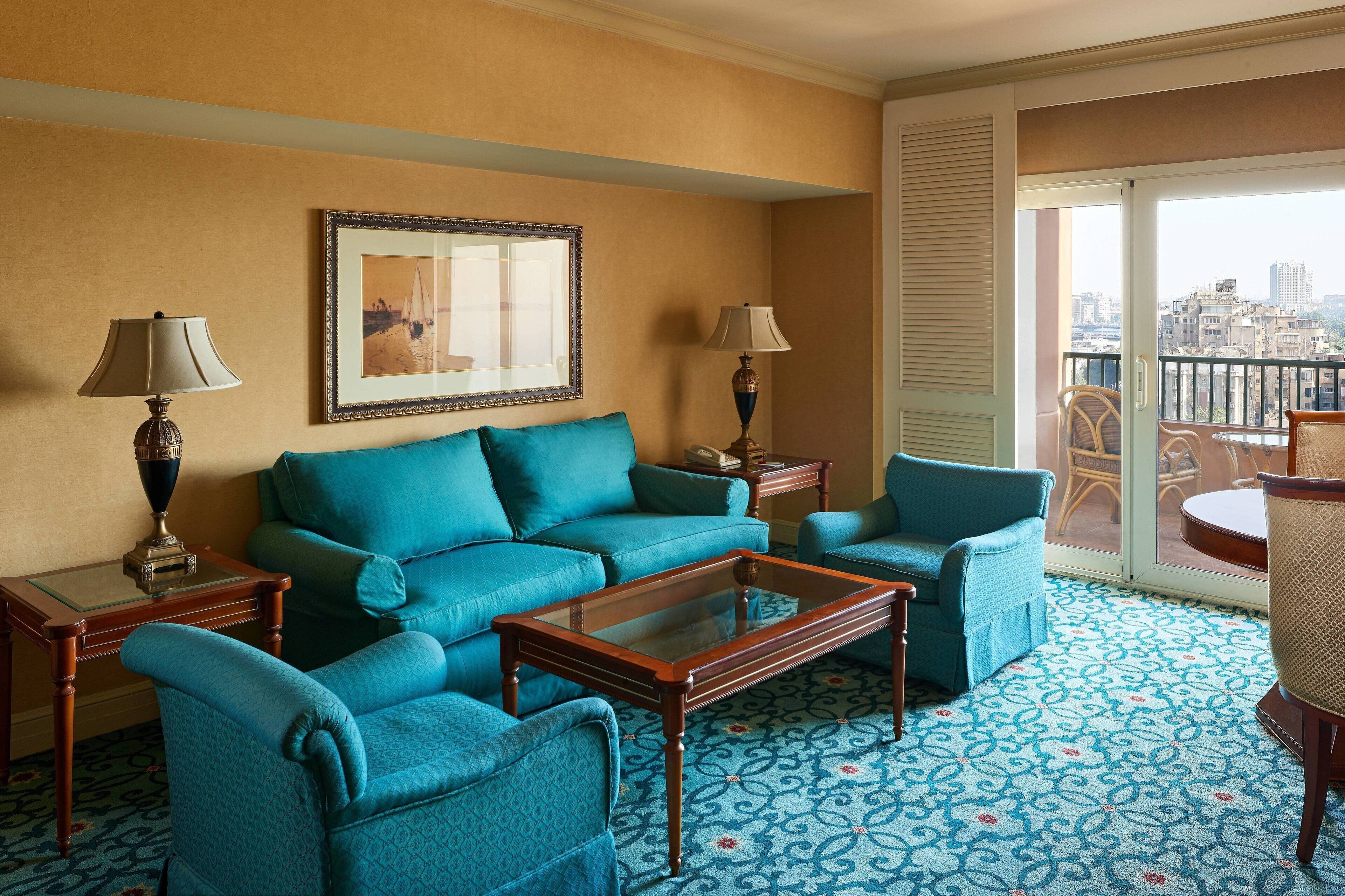 A hotel room with a blue patterned carpet, a sofa, a coffee table, and two lamps.