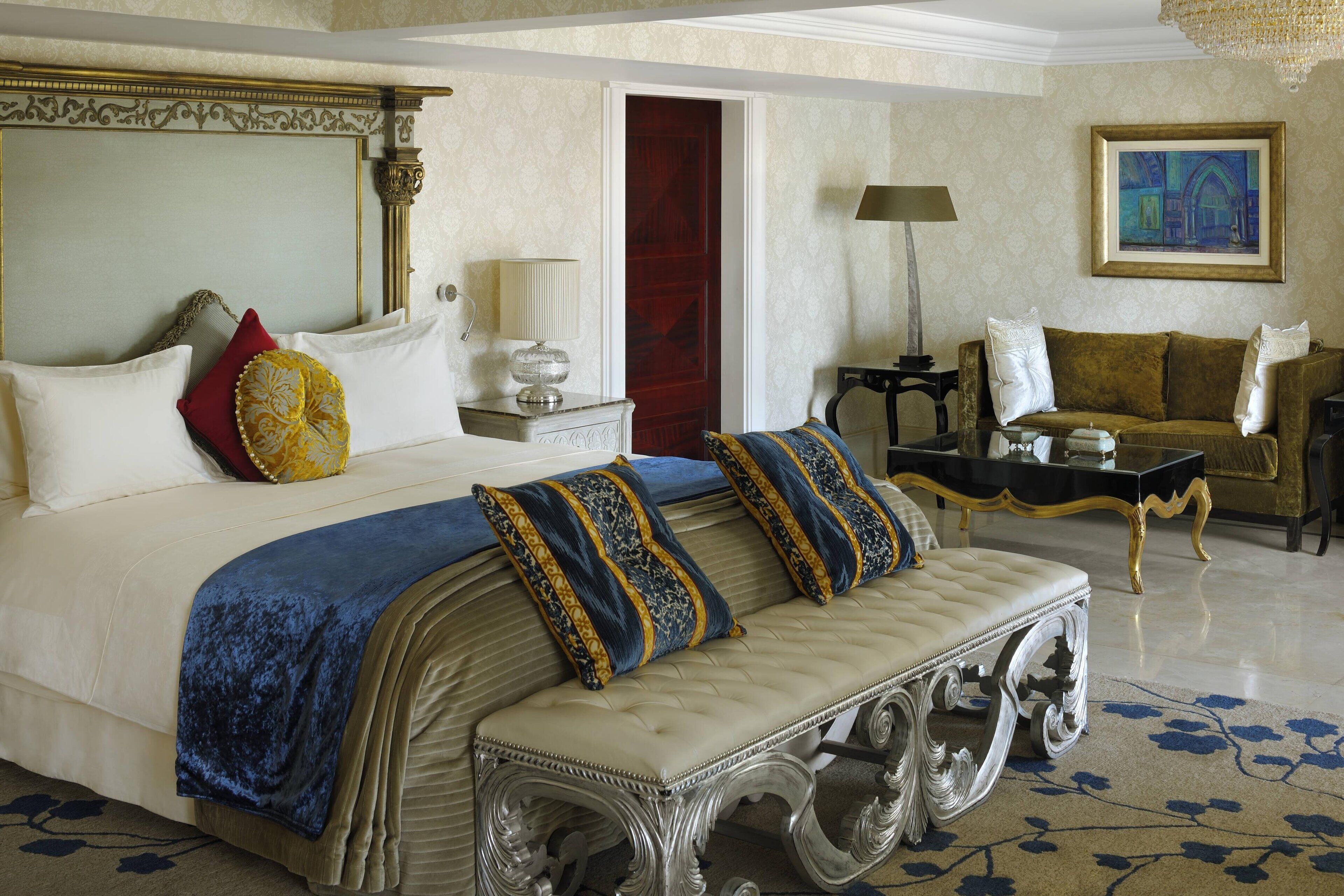 A luxurious bedroom with a large bed, a chaise lounge, a sofa, and a painting on the wall.