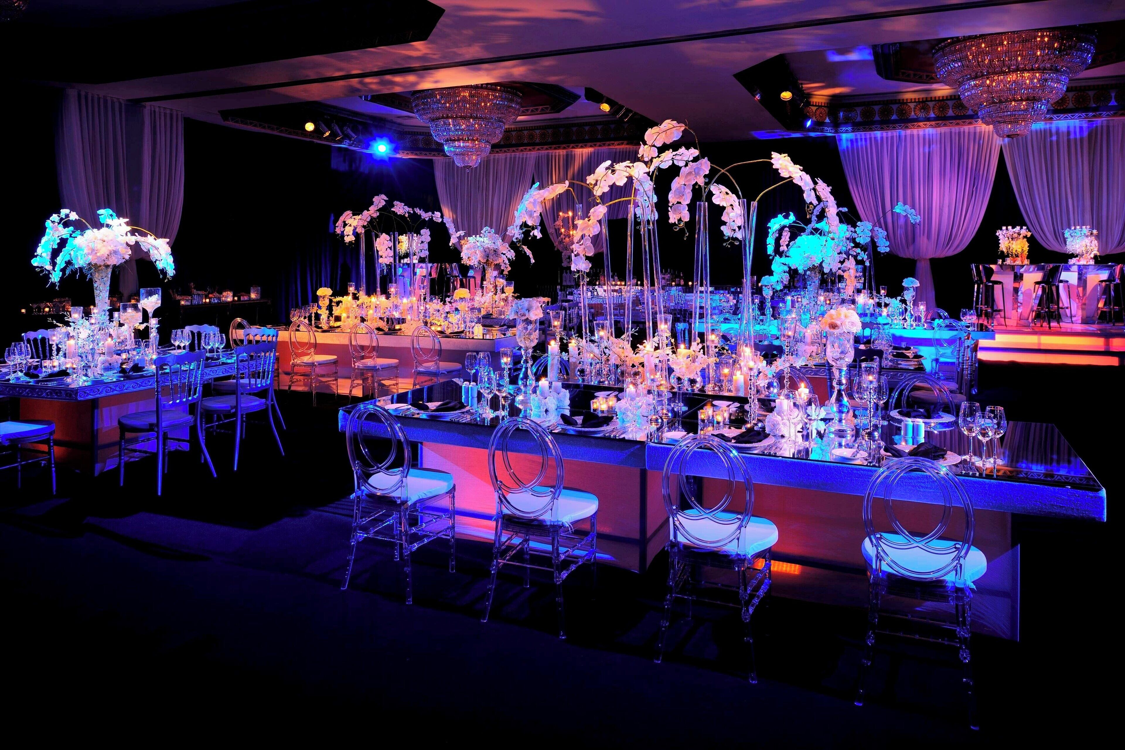 A luxurious banquet hall with a long dining table, clear chairs, and elegant floral centerpieces.